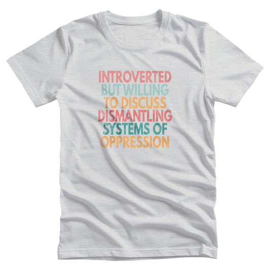 Ash color unisex t-shirt that says, “Introverted But Willing to Discuss Dismantling Systems of Oppression” spread out in 6 rows with each row a different color. “Introverted” is red/dark pink, “But Willing” is blue-green, “To Discuss” is yellow/orange, “Dismantling” is red/dark pink, “Systems of” is a dark blue-green, and “Oppression” is yellow/orange. The text has a slightly distressed look.