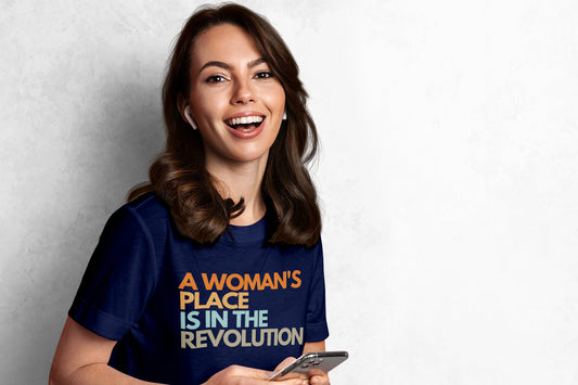 A young woman wearing a navy blue t-shirt that says, "A woman's place is in the revolution" in all caps.