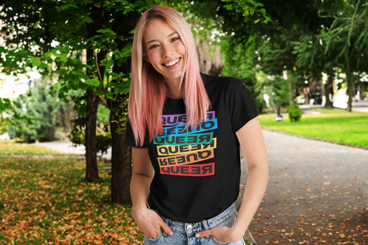 A smiling woman with blonde and pink hair standing outside wearing a shirt that says "Queer" in various, fun iterations.