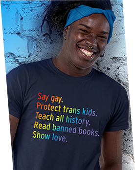 A man of color wearing a t-shirt promoting inclusivity that says, "Say gay. Protect Trans Kids. Teach all history. Read banned books. Show love." in rainbow colors. 