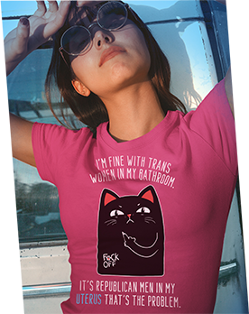 A woman wearing a shirt that says, “I’M FINE WITH TRANS WOMEN IN MY BATHROOM” with an illustration of a cat underneath it holding up its middle claw. Under that, it says, “IT’S REPUBLICAN MEN IN MY UTERUS THAT’S THE PROBLEM.”