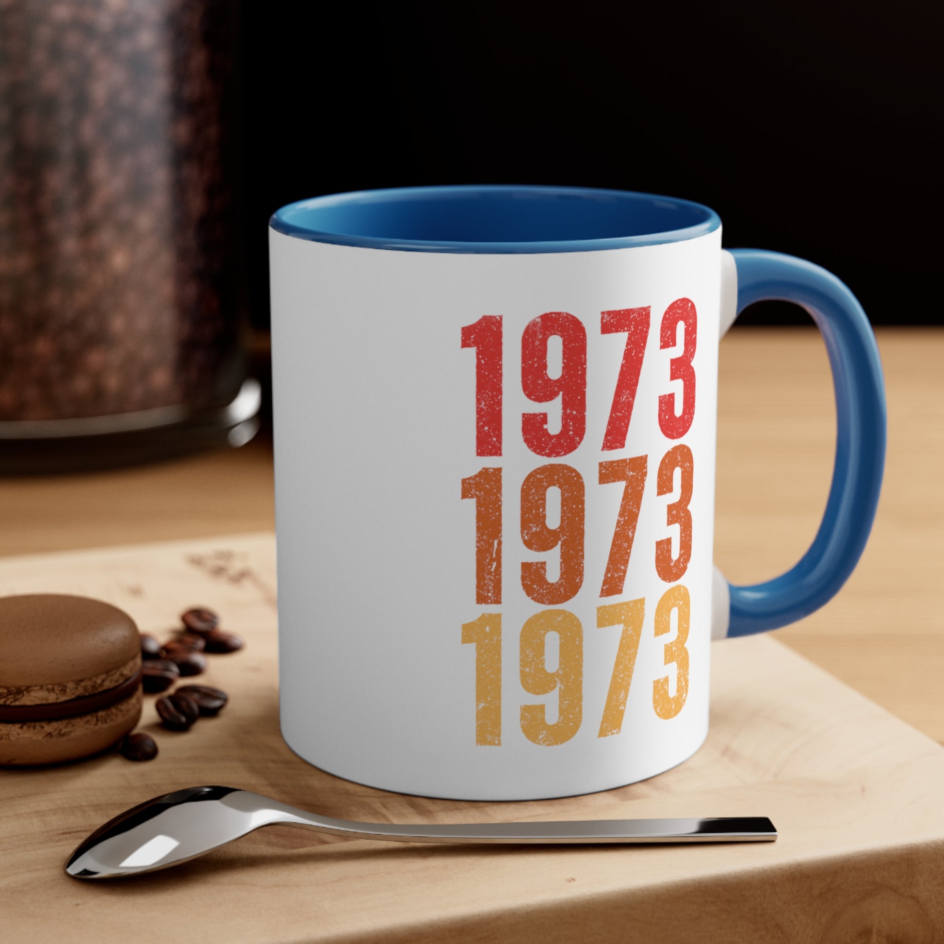 Contextual image of an 11oz ceramic mug with a blue interior and handle featuring retro-inspired colors and slight distressing, repeated three times in distinct rows. The mug is on a table with a spoon and a cookie.