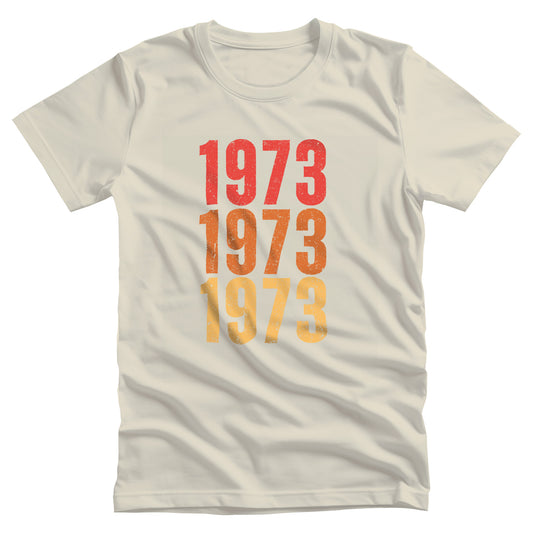 Natural color vintage-style unisex t-shirt with ‘1973” on the front, featuring retro-inspired colors and slight distressing, repeated three times in distinct rows.