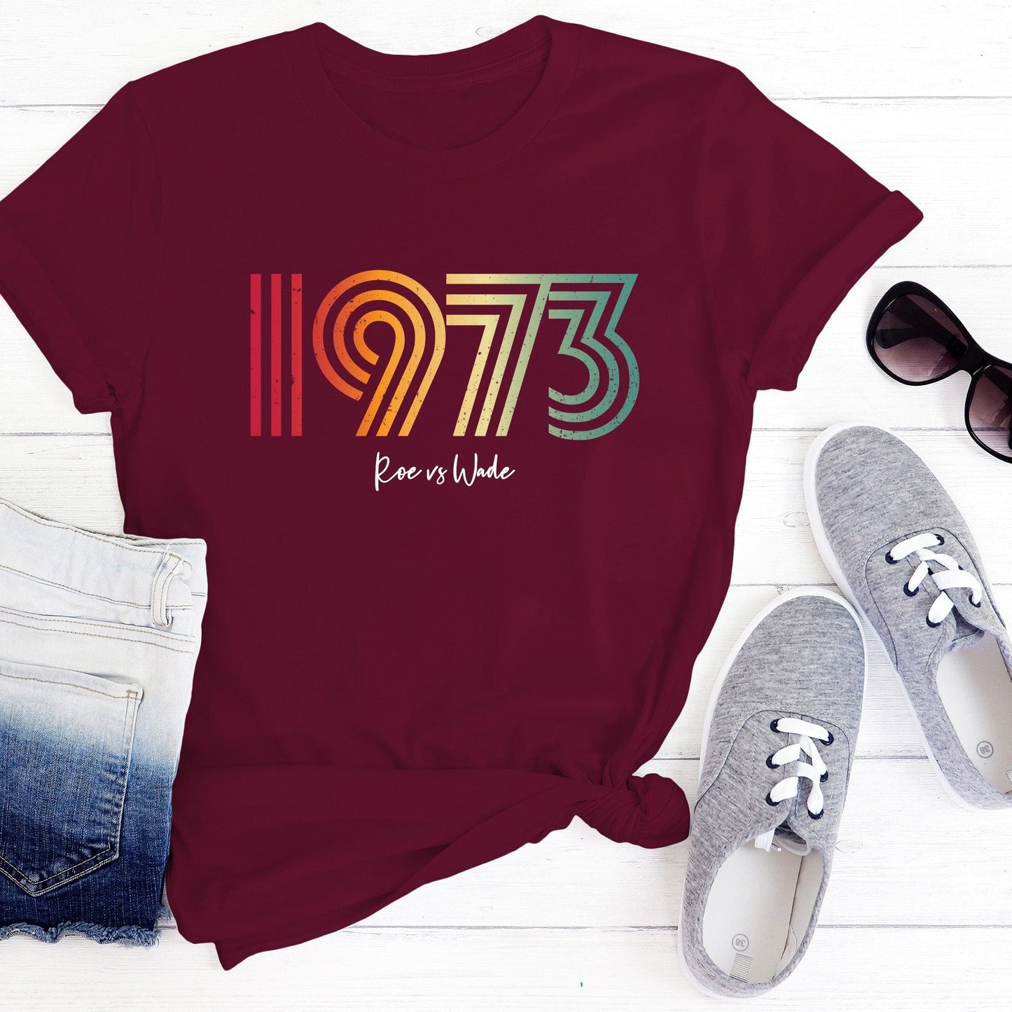 Maroon unisex t-shirt that says, “1973 Roe vs Wade.” The numbers are in a round, lined retro font in a rainbow-gradient color. “Roe vs Wade” is beneath it in a script font.