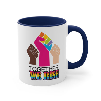 Navy Blue accented 11oz ceramic mug ]with a graphic a brown skin-colored fist on the left, a rainbow fist front and center, and a white skin-colored fist on the right. Below that reads “Together We Rise.” “Together” is on one line and “We Rise” is below that in rainbow colors. The inside of the mug and the handle are both navy blue.