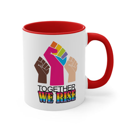 Red accented 11oz ceramic mug ]with a graphic a brown skin-colored fist on the left, a rainbow fist front and center, and a white skin-colored fist on the right. Below that reads “Together We Rise.” “Together” is on one line and “We Rise” is below that in rainbow colors. The inside of the mug and the handle are both red.