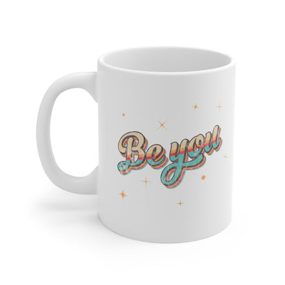 11oz white ceramic mug that says “Be you” in a vintage-inspired script font with vintage colors and stripes. It’s designed to look as if small parts of the design are coming off of the mug.