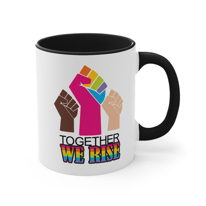 Black accented 11oz ceramic mug ]with a graphic a brown skin-colored fist on the left, a rainbow fist front and center, and a white skin-colored fist on the right. Below that reads “Together We Rise.” “Together” is on one line and “We Rise” is below that in rainbow colors. The inside of the mug and the handle are both black.