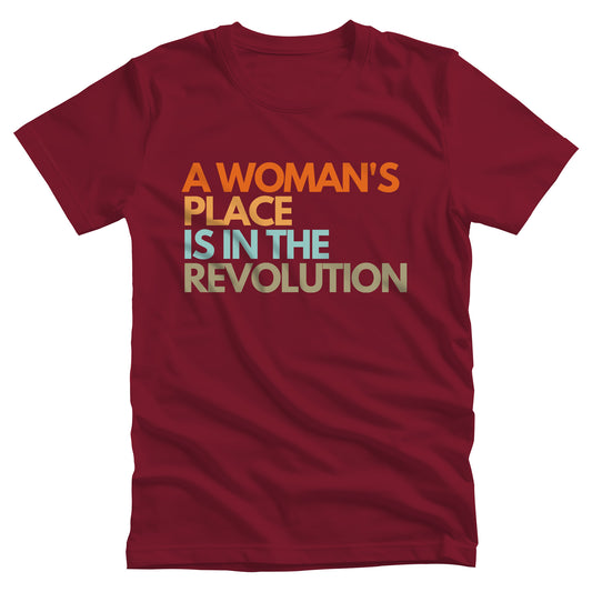 Cardinal color unisex t-shirt that says “A woman’s place is in the revolution” in a round, modern font in all caps and left aligned. Each line is a different color. “A Woman’s” is orange, “place” is yellow-orange, “is in the” is light blue, and “revolution” is military green.