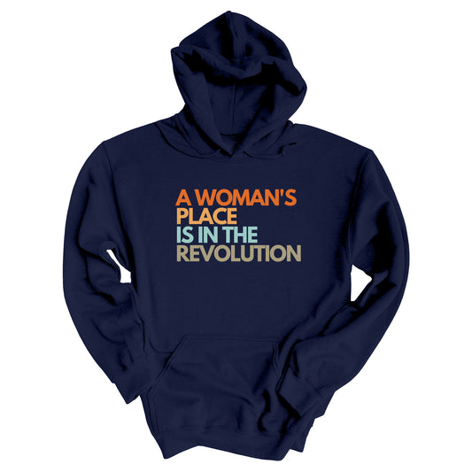 Navy Blue hoodie that says “A woman’s place is in the revolution” in a round, modern font in all caps and left aligned. Each line is a different color. “A Woman’s” is orange, “place” is yellow-orange, “is in the” is light blue, and “revolution” is military green.