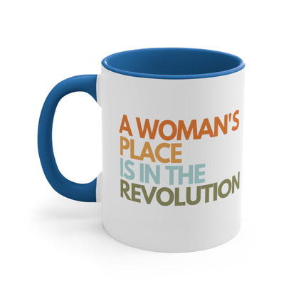 11oz ceramic mug with a blue interior and handle that says “A woman’s place is in the revolution” in a round, modern font in all caps and left aligned. Each line is a different color. “A Woman’s” is orange, “place” is yellow-orange, “is in the” is light blue, and “revolution” is military green.