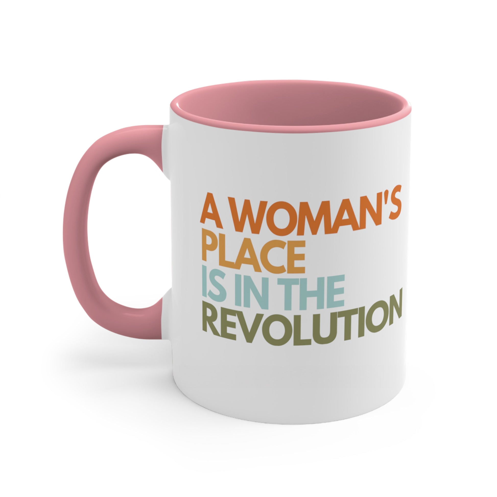 11oz ceramic mug with a pink interior and handle that says “A woman’s place is in the revolution” in a round, modern font in all caps and left aligned. Each line is a different color. “A Woman’s” is orange, “place” is yellow-orange, “is in the” is light blue, and “revolution” is military green.