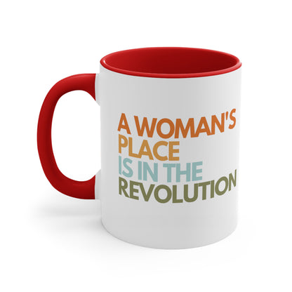 11oz ceramic mug with a red interior and handle that says “A woman’s place is in the revolution” in a round, modern font in all caps and left aligned. Each line is a different color. “A Woman’s” is orange, “place” is yellow-orange, “is in the” is light blue, and “revolution” is military green.