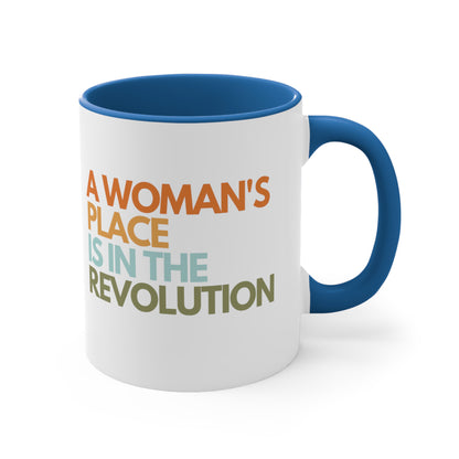 11oz ceramic mug with a blue interior and handle that says “A woman’s place is in the revolution” in a round, modern font in all caps and left aligned. Each line is a different color. “A Woman’s” is orange, “place” is yellow-orange, “is in the” is light blue, and “revolution” is military green.