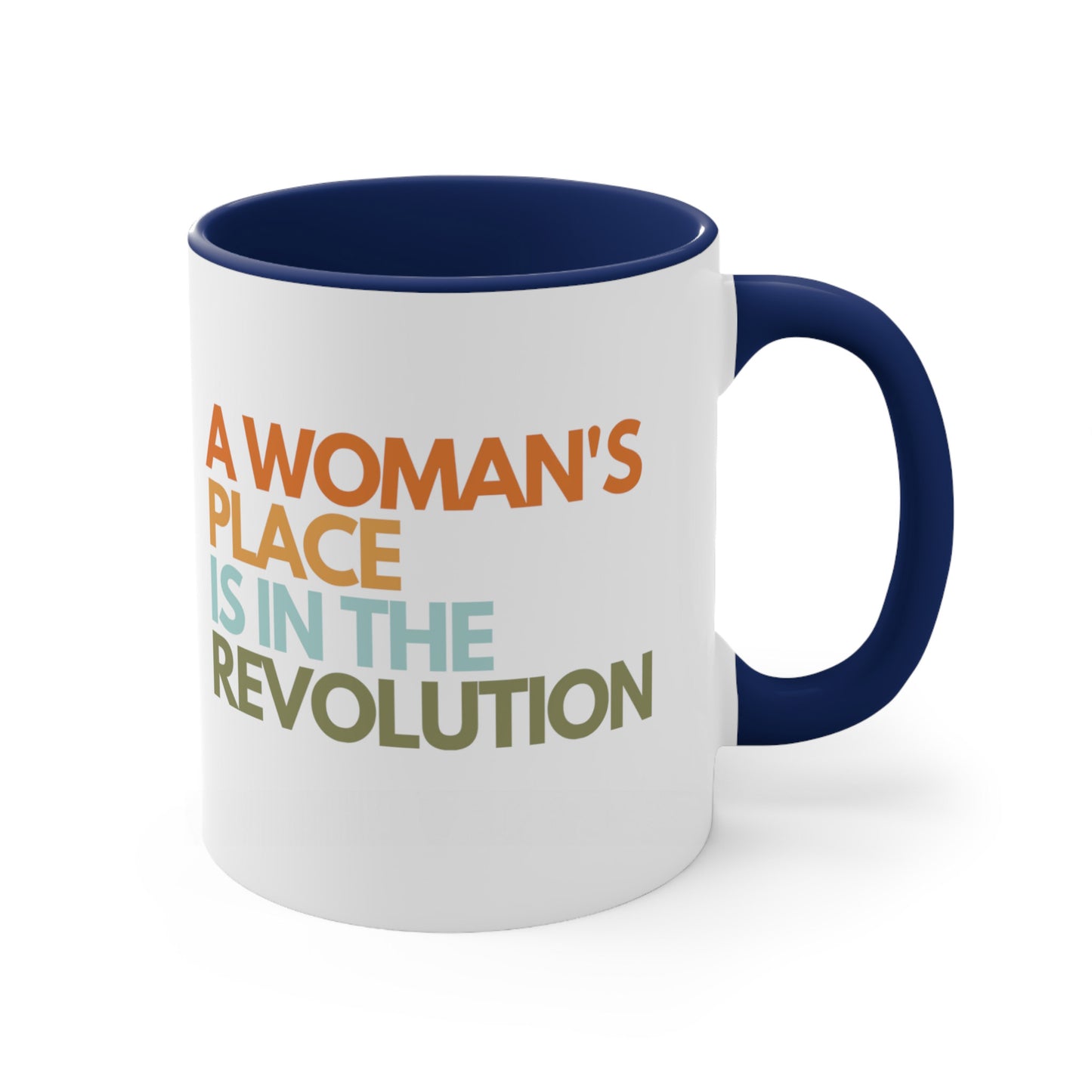 11oz ceramic mug with a navy blue interior and handle that says “A woman’s place is in the revolution” in a round, modern font in all caps and left aligned. Each line is a different color. “A Woman’s” is orange, “place” is yellow-orange, “is in the” is light blue, and “revolution” is military green.