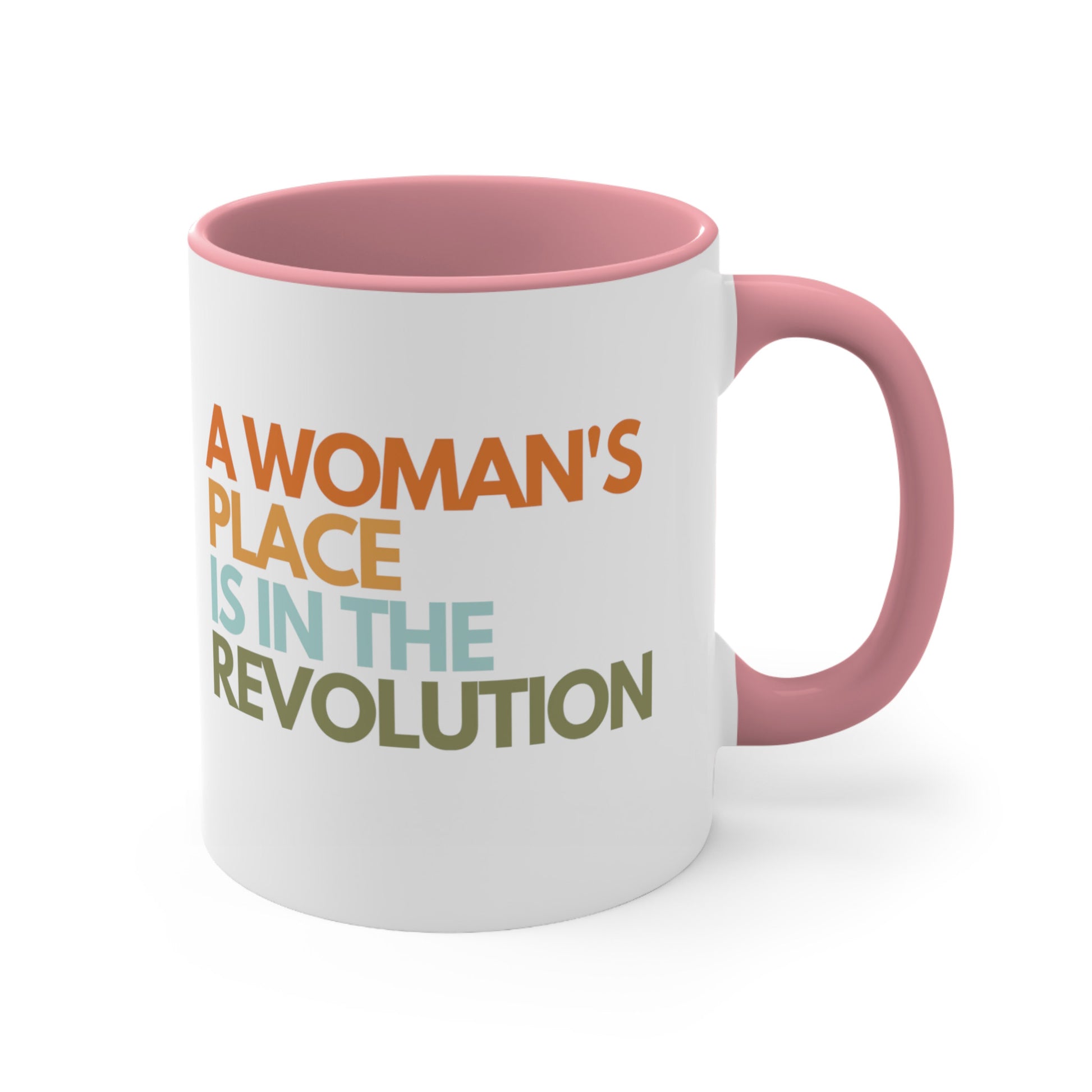 11oz ceramic mug with a pink interior and handle that says “A woman’s place is in the revolution” in a round, modern font in all caps and left aligned. Each line is a different color. “A Woman’s” is orange, “place” is yellow-orange, “is in the” is light blue, and “revolution” is military green.