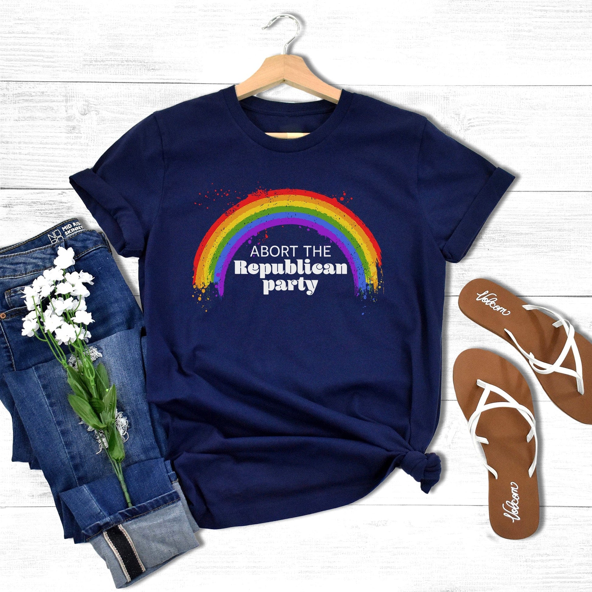 Navy Blue unisex t-shirt with a graphic of a rainbow with small paint splatters around it. Inside the negative space of the rainbow is the text, “Abort the Republican Party.” 