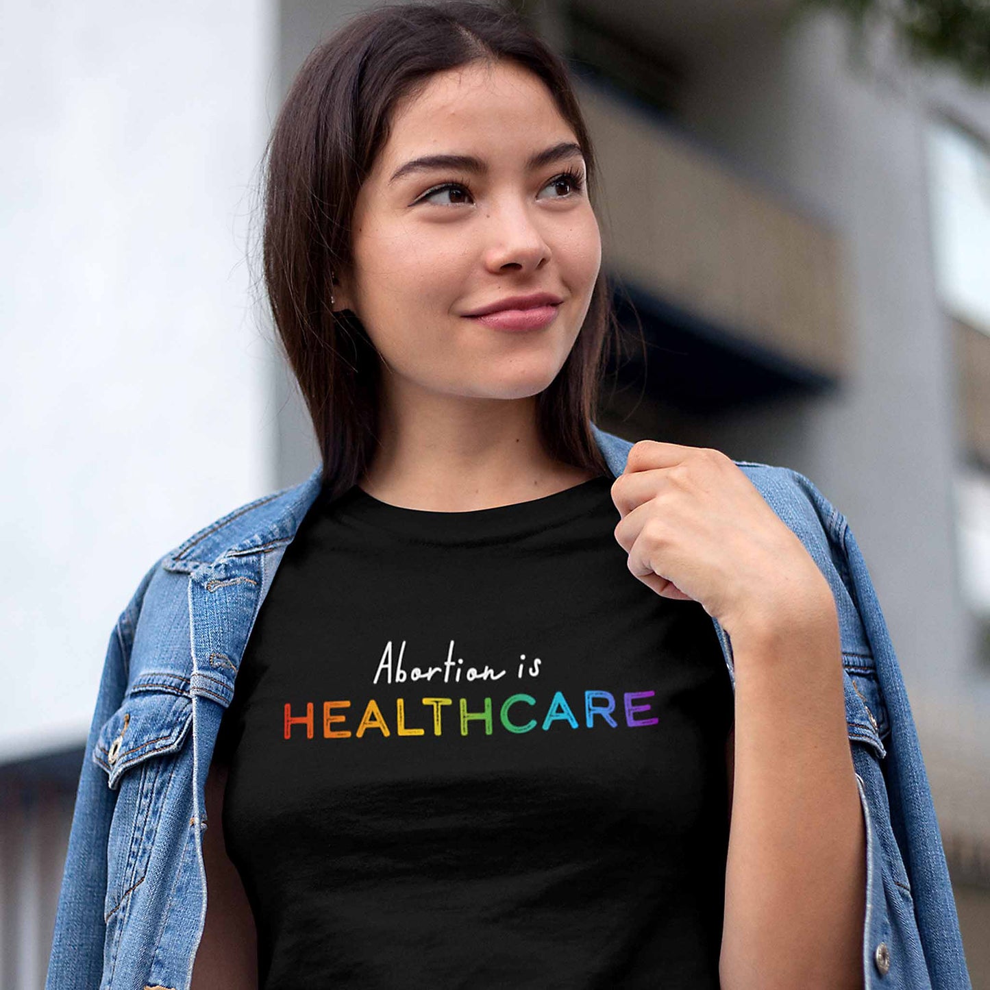 Black unisex t-shirt that says, “Abortion is Healthcare.” The words “Abortion is” is in a script font, and “Healthcare” is in all caps in a rainbow gradient color.