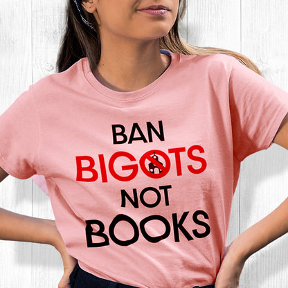 Pink unisex t-shirt that says, “Ban Bigots Not Books” in all caps. Each word is on its own line. The word “Bigots” is red and the “O” has a line illustration of a church inside it with a slash to cross it out.