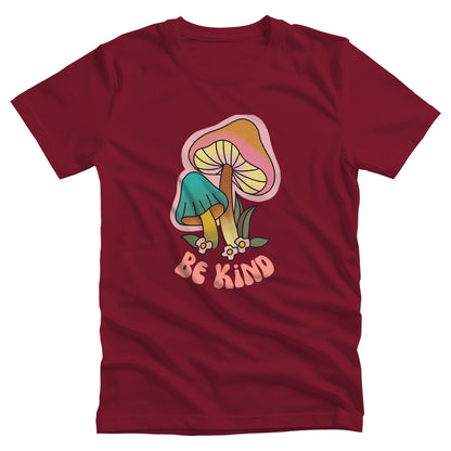 Cardinal color unisex t-shirt that says “Be Kind” in a retro font with two retro mushrooms above the text. The text is slightly arched down.