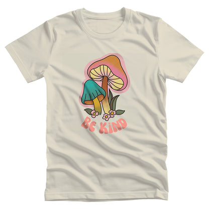 Natural color unisex t-shirt that says “Be Kind” in a retro font with two retro mushrooms above the text. The text is slightly arched down.