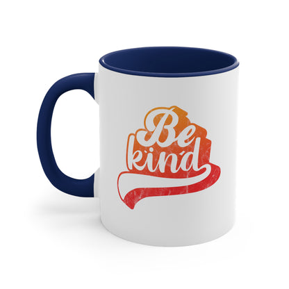 11oz ceramic mug with a navy blue handle and interior that says, “Be Kind” in a script font that is an orange gradient color. The “d” has a unique swoosh glyph extending below the word, adding a dynamic and flowing aesthetic to the text.