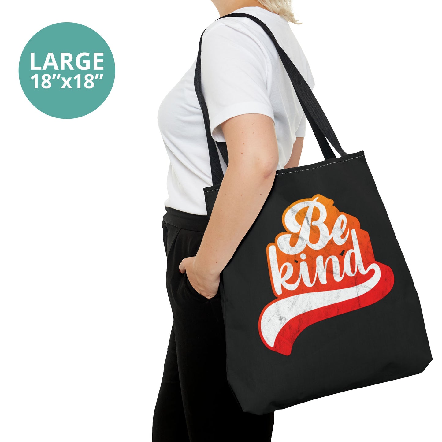 Contextual photo of a woman holding a large 18x18”black tote bag that says, “Be Kind” in a script font that has an orange gradient. The “d” has a unique swoosh glyph extending below the word, adding a dynamic and flowing aesthetic to the text.