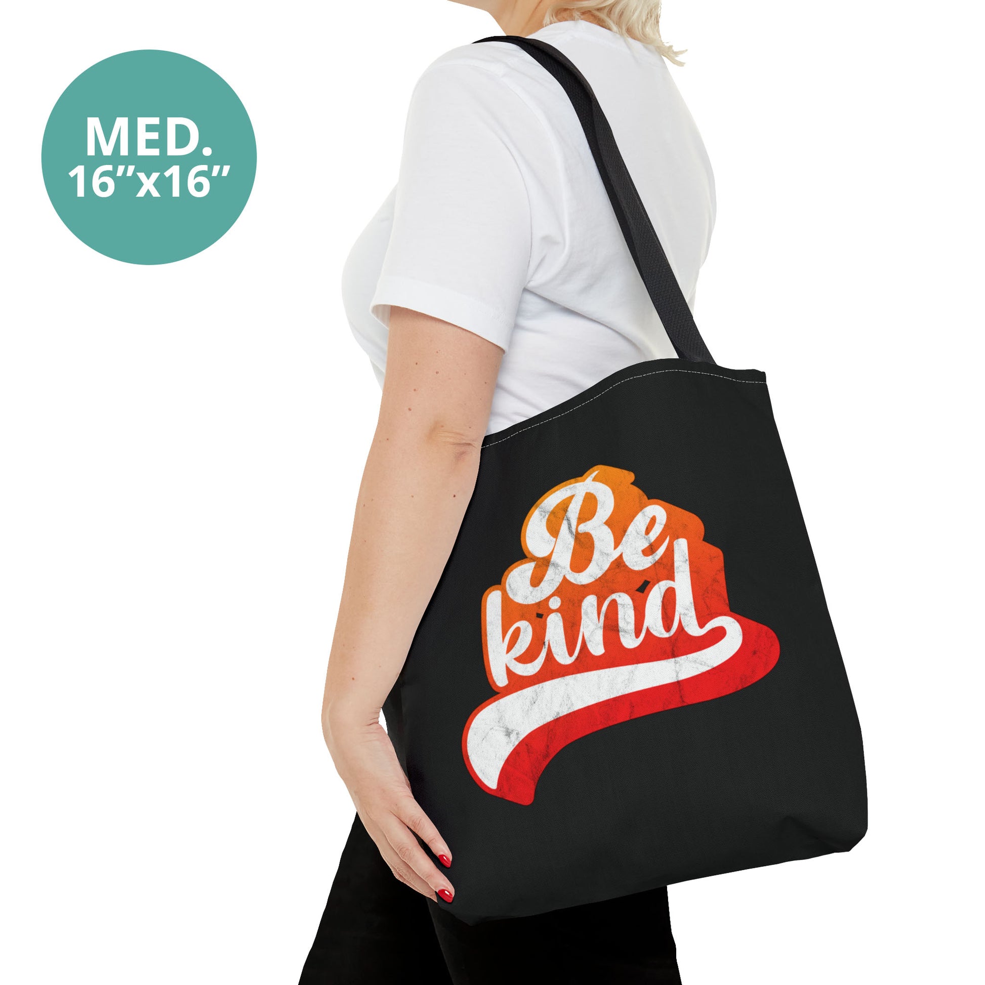 Contextual photo of a woman holding a medium 16x16” black tote bag that says, “Be Kind” in a script font that has an orange gradient. The “d” has a unique swoosh glyph extending below the word, adding a dynamic and flowing aesthetic to the text.