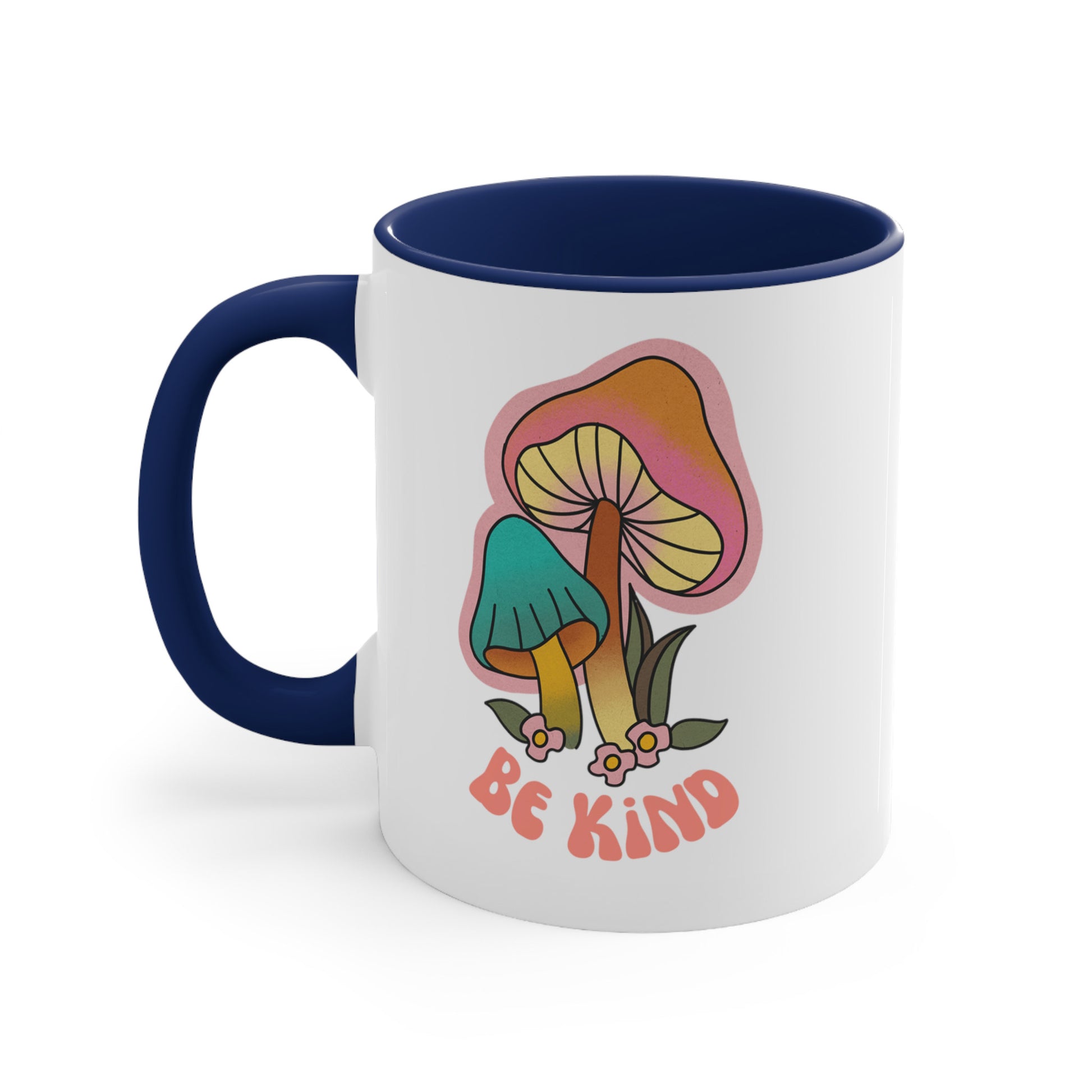 11oz ceramic mug with a navy blue handle and interior that says “Be Kind” on the front in a retro font with two retro mushrooms above the text. The text is slightly arched down.