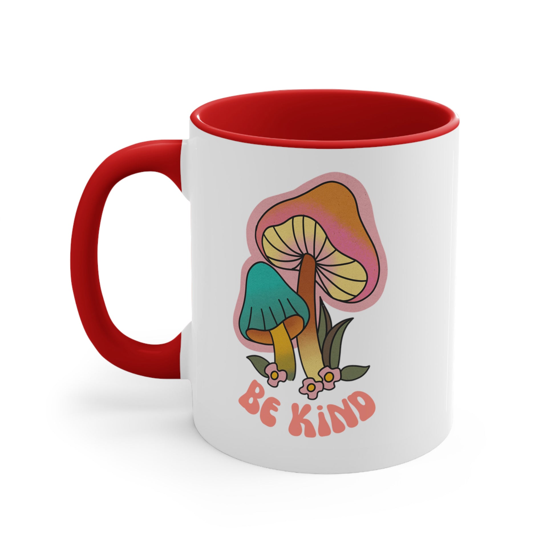 11oz ceramic mug with a red handle and interior that says “Be Kind” on the front in a retro font with two retro mushrooms above the text. The text is slightly arched down.