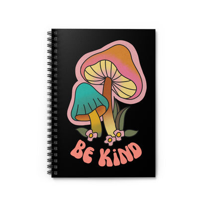 Black spiral notebook that says “Be Kind” on the front in a retro font with two retro mushrooms above the text. The text is slightly arched down.