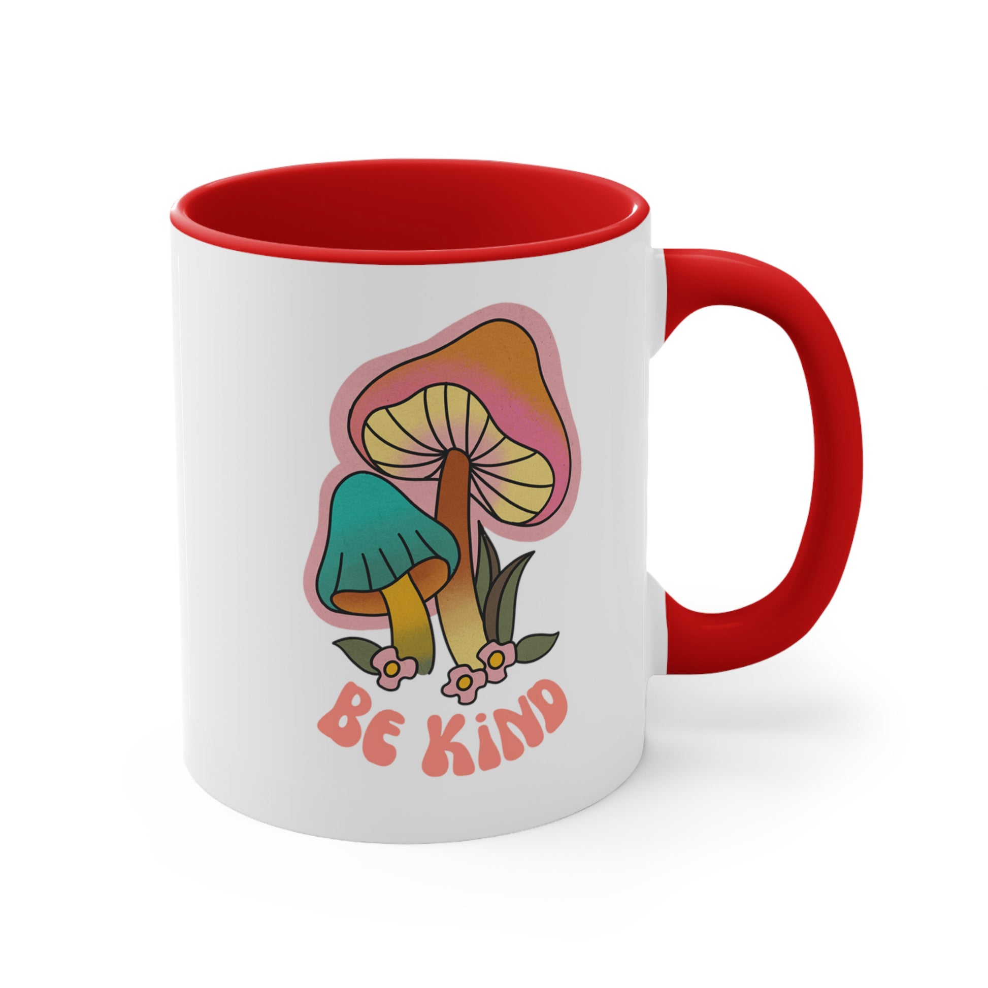 11oz ceramic mug with a red handle and interior that says “Be Kind” on the front in a retro font with two retro mushrooms above the text. The text is slightly arched down.