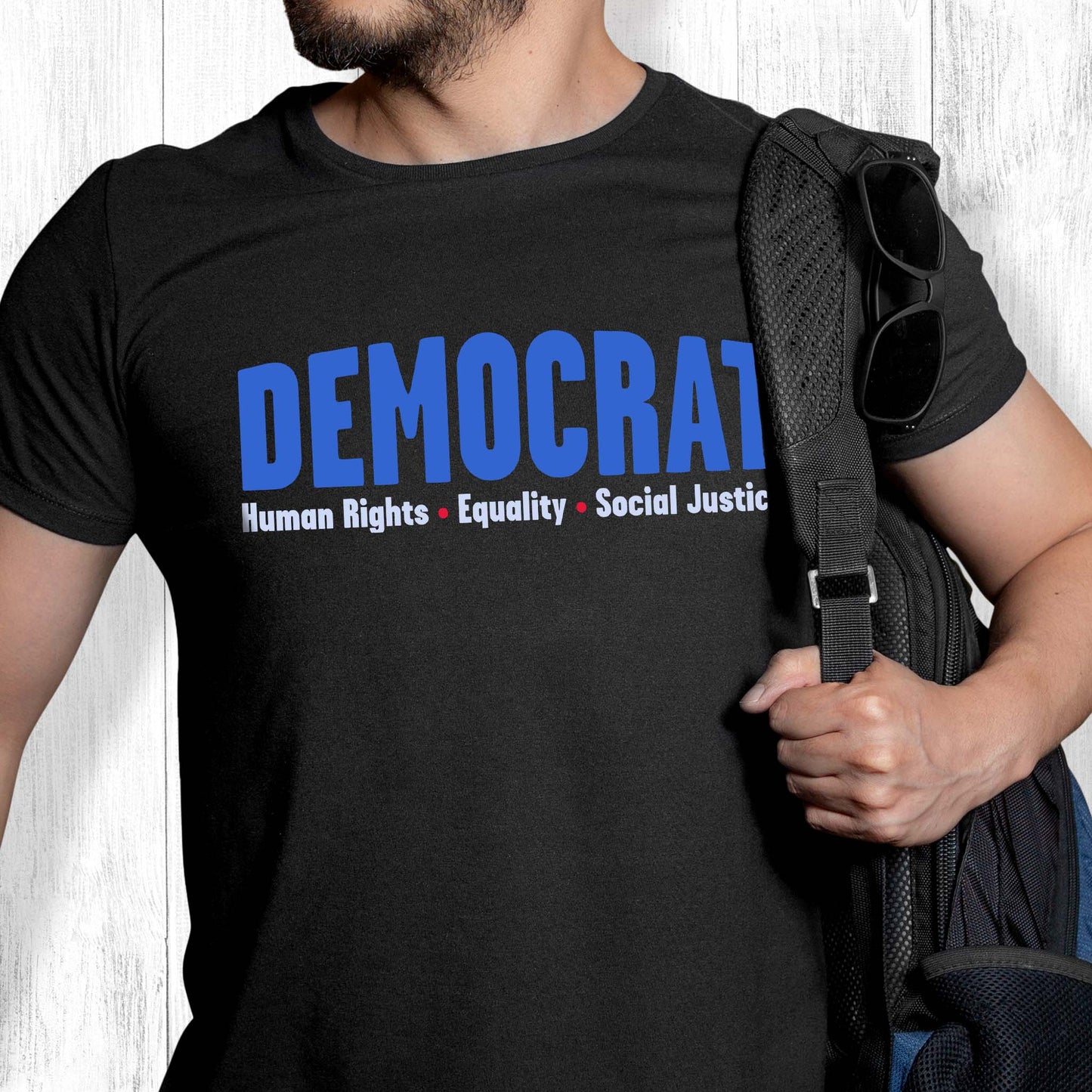 Black unisex t-shirt that says, “DEMOCRAT: Human Rights, Equality, Social Justice” with the word “DEMOCRAT” being large and slightly arced upwards. The rest of the text is in a single line below with red dots between them.