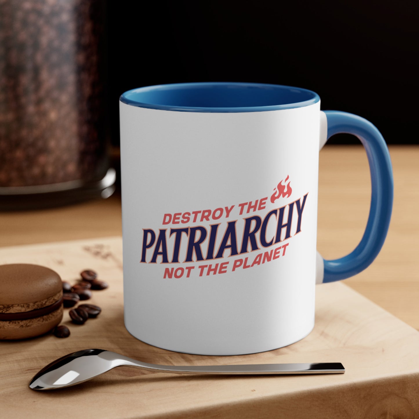 Contextual image of an 11oz ceramic mug with a blue interior and handle with text: 'DESTROY THE PATRIARCHY NOT THE PLANET slanted upwards. 'DESTROY THE' is on the first line with small flames after it, 'PATRIARCHY' is on the second line, and 'NOT THE PLANET' is on the third line.