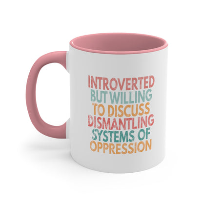 11oz ceramic mug with a pink interior and handle with a graphic that says “Introverted but willing to discuss dismantling systems of oppression.” The graphic is slightly distressed, and each line of the graphic is a different color.