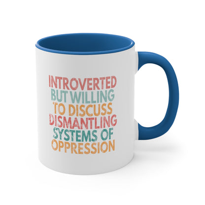 11oz ceramic mug with a blue color interior and handle with a graphic that says “Introverted but willing to discuss dismantling systems of oppression.” The graphic is slightly distressed, and each line of the graphic is a different color.