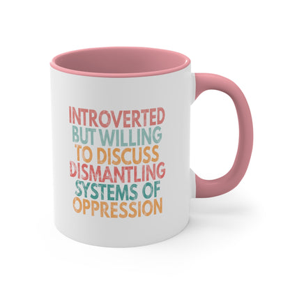 11oz ceramic mug with a pink interior and handle with a graphic that says “Introverted but willing to discuss dismantling systems of oppression.” The graphic is slightly distressed, and each line of the graphic is a different color.