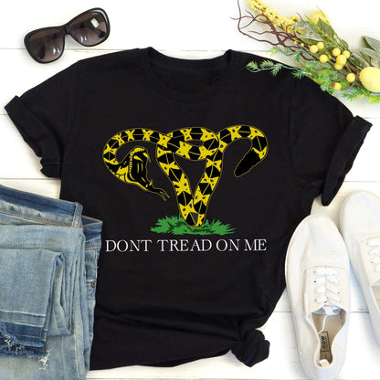 Black unisex t-shirt with an image of a rattlesnake coiled into the shape of a uterus. Its mouth is wide open ready to strike. Beneath the graphic, it says, “DONT TREAD ON ME” with no apostrophe in “DON’T” like the original.