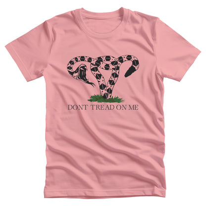 Pink unisex t-shirt with an image of a rattlesnake coiled into the shape of a uterus. Its mouth is wide open ready to strike. Beneath the graphic, it says, “DONT TREAD ON ME” with no apostrophe in “DON’T” like the original.