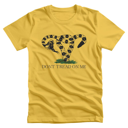 Yellow unisex t-shirt with an image of a rattlesnake coiled into the shape of a uterus. Its mouth is wide open ready to strike. Beneath the graphic, it says, “DONT TREAD ON ME” with no apostrophe in “DON’T” like the original.