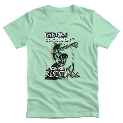 Heather Mint color unisex t-shirt featuring the phrase 'Embrace Coexistence or Brace for Resistance' in a grunge font. The shirt includes an illustration of a cat meowing loudly with a small crown to the right, adding to the grunge aesthetic. Small red letters along the left side of the cat's face, written vertically say, ‘Kindness is revolutionary' in all caps.