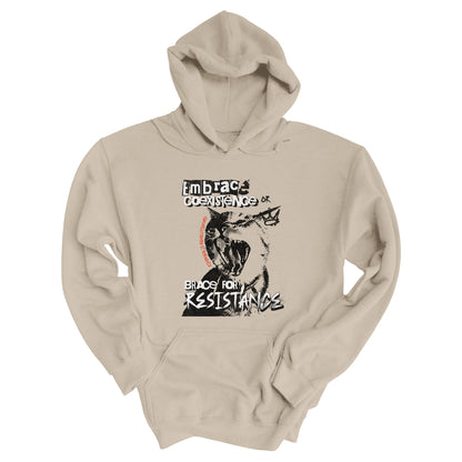 Sand color hoodie featuring the phrase 'Embrace Coexistence or Brace for Resistance' in a grunge font. The shirt includes an illustration of a cat meowing loudly with a small crown to the right, adding to the grunge aesthetic. Small red letters along the left side of the cat's face, written vertically say, ‘Kindness is revolutionary' in all caps.