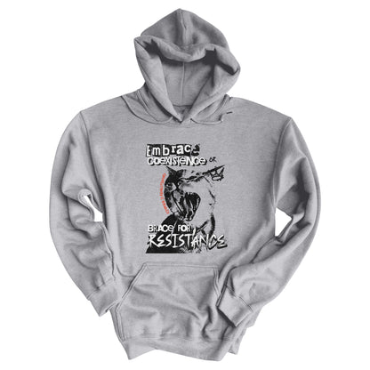 Sport Grey color hoodie featuring the phrase 'Embrace Coexistence or Brace for Resistance' in a grunge font. The shirt includes an illustration of a cat meowing loudly with a small crown to the right, adding to the grunge aesthetic. Small red letters along the left side of the cat's face, written vertically say, ‘Kindness is revolutionary' in all caps.