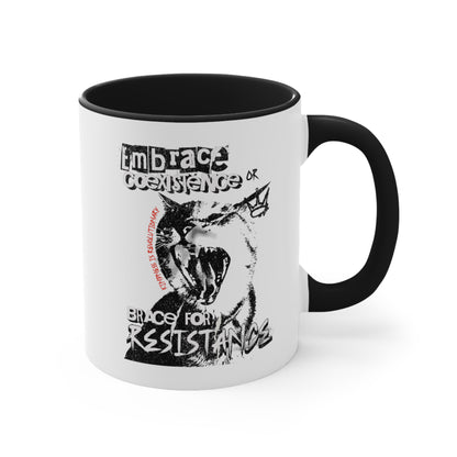 11oz ceramic mug with a black interior and handle featuring the phrase 'Embrace Coexistence or Brace for Resistance' in a grunge font. The shirt includes an illustration of a cat meowing loudly with a small crown to the right, adding to the grunge aesthetic. Small red letters along the left side of the cat's face, written vertically say, ‘Kindness is revolutionary' in all caps.