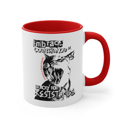 11oz ceramic mug with a red interior and handle featuring the phrase 'Embrace Coexistence or Brace for Resistance' in a grunge font. The shirt includes an illustration of a cat meowing loudly with a small crown to the right, adding to the grunge aesthetic. Small red letters along the left side of the cat's face, written vertically say, ‘Kindness is revolutionary' in all caps.