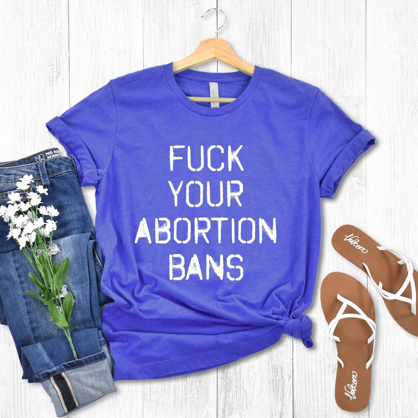 Heather True Royal color unisex t-shirt that says, “FUCK YOUR ABORTION BANS” in a stencil font with ink bleeding slightly outside of the text.