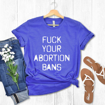 Heather True Royal color unisex t-shirt that says, “FUCK YOUR ABORTION BANS” in a stencil font with ink bleeding slightly outside of the text.