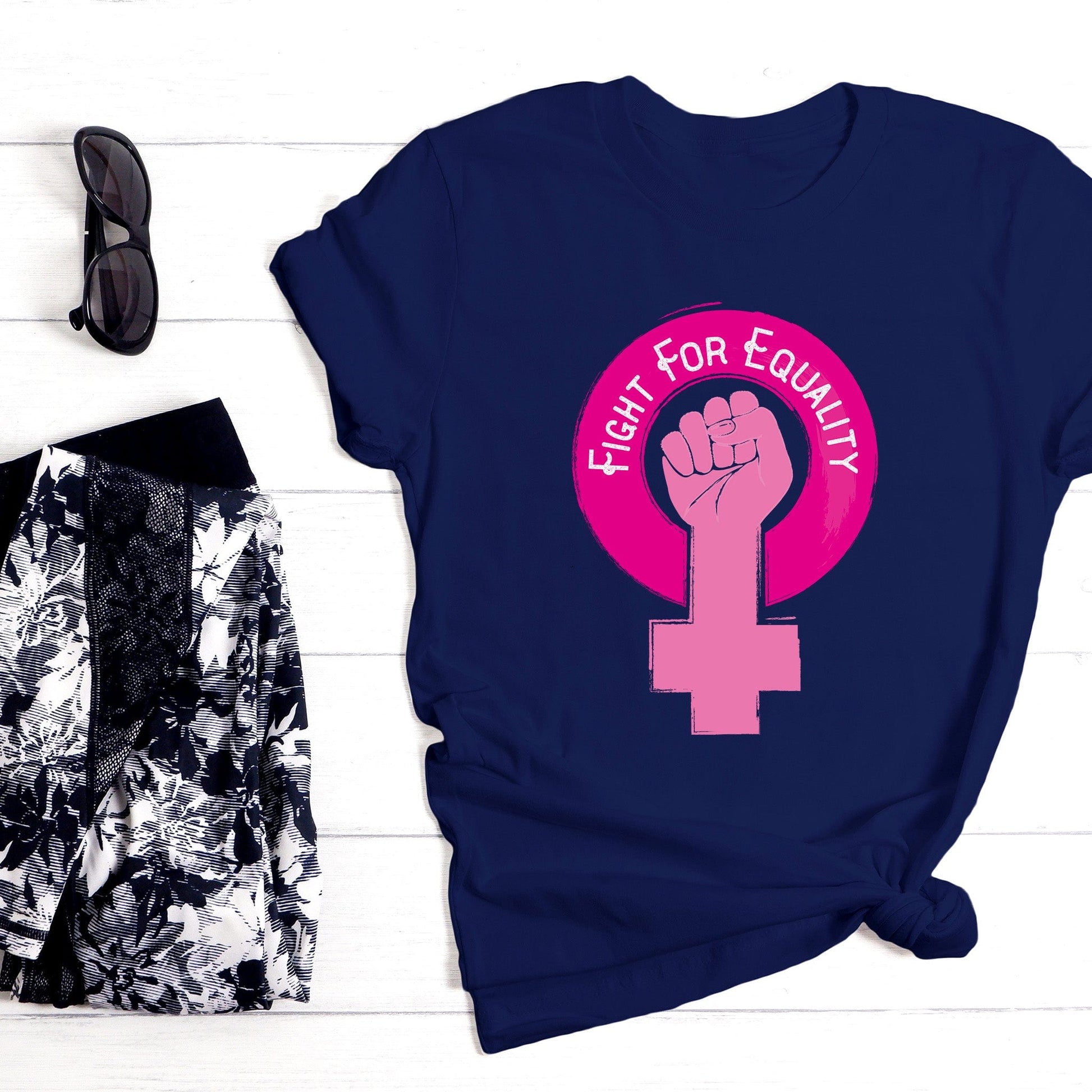 Navy Blue unisex t-shirt that says, “Fight for Equality” arched inside a pink gender symbol for women. The “T” in the symbol is in the shape of a fist.