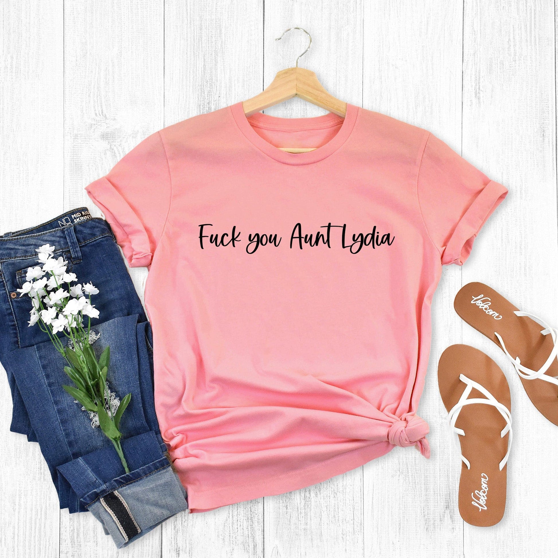 Pink unisex t-shirt that says, “Fuck you, Aunt Lydia” in a script font.