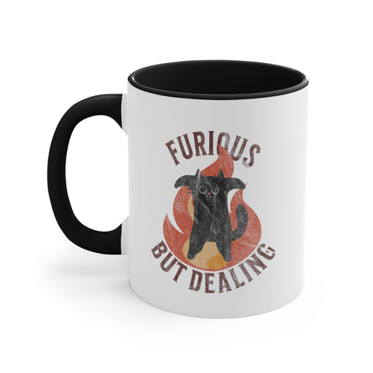 11oz ceramic mug with a black interior and handle that says “Furious but dealing” in all caps. The word “furious” is arched over an image of an angry black cat standing up on its hind legs with its arms spread with a large flame behind it. “But Dealing” is arched the opposite way underneath the graphic. The graphic is retro-inspired with a worn look.